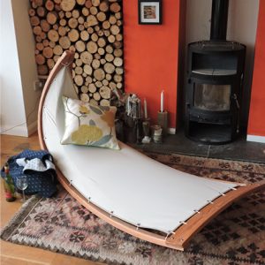 Photo of Hang-In-Out's reverse rocking chair in front of a woodburner and log pile.