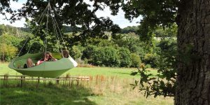 Hang-In-Out's large leaf green Lullio Cacoon hanging from a tree with a group of people enjoying the relaxing comfort