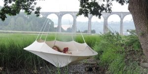 Hang-In-Out's large natural white Lullio Cacoon hanging from a tree with a lady looking extremely relaxed and comfortable enjoying some time alone in a beautiful creekside setting with a fabulous viaduct backdrop