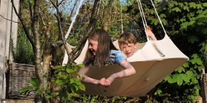 Hang-In-Out's medium natural white Lullio Cacoon hanging from a garden frame with two children enjoying themselves swaying gently in their spaceship!